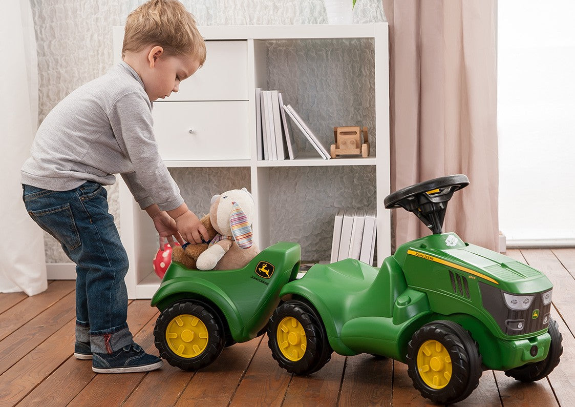 Lifestyle image of child using foot to floor resin tractor to transport stuffed animals 
